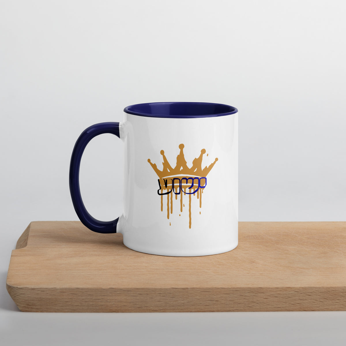 11 oz | Front view of white and blue Yeshua King ceramic coffee mug on a wooden board, featuring ישוע in Hebrew beneath a dripping gold crown with blue handle, rim, and interior.